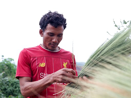 Ein Mann hält ein Bündel Gras in der Hand und verknotet die Enden