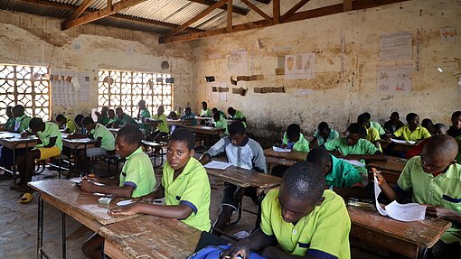 Schüler sitzen in einem spärlich eingerichteten Klassenzimmer und lernen