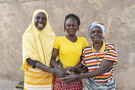 Drei Frauen aus drei Generationen stehen nebeneinander und halten sich gemeinsam an den Händen