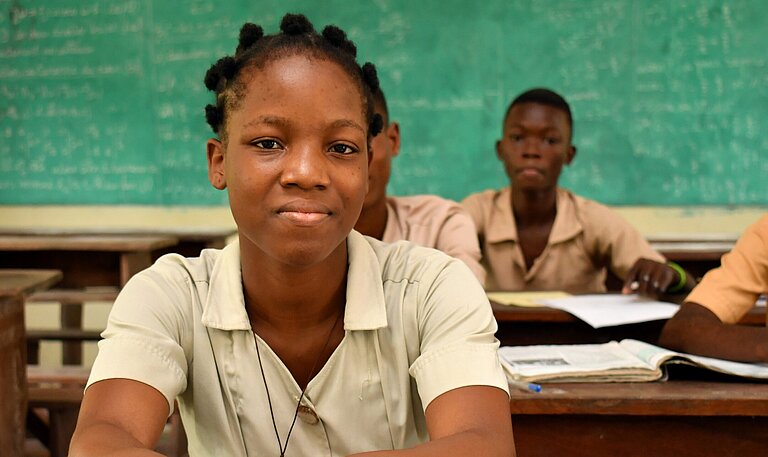 Monique sitzt an ihrem Platz im Klassenzimmer und folgt dem Unterricht