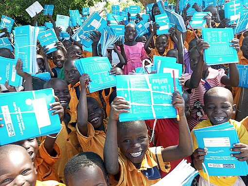 Schulkinder in West Nile halten lachend neue Schulmaterialien in die Kamera