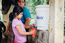 Ein Mädchen nutzt den Wasserspender von Plan International nach einem Hurrikan