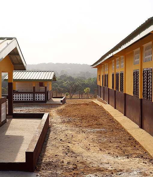 Gelb-braunes, neues Schulgebäude mit Waldlandschaft im Hintergrund