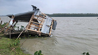 Die Überreste eines Hauses werden von einer Überschwemmung langsam in den Fluss gezogen.