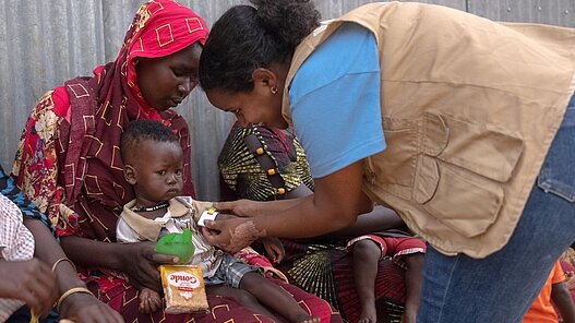 Plan International Mitarbeiterin untersucht kleinen Jungen auf Unterernährung