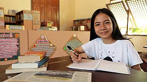 Bild: Ein junges Mädchen sitzt in der Schule und schreibt in ein Buch.
