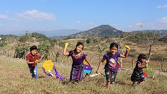 Vier Kinder laufen über einen Hügel und ziehen Drachen hinter sich her