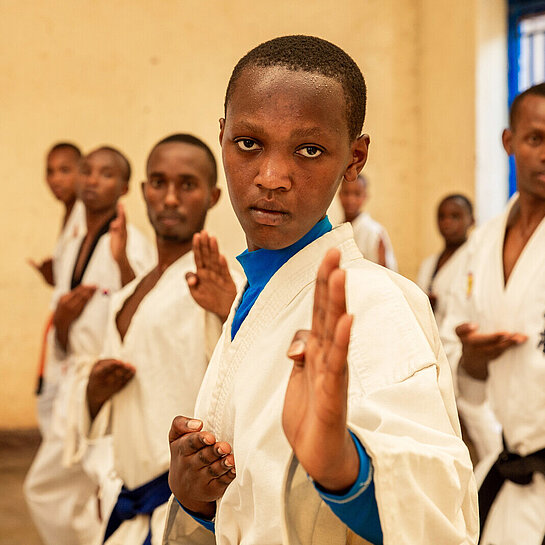 Eine Gruppe Jugendlicher in Karate-Anzügen schaut konzentriert in die Kamera, Hände gehoben.