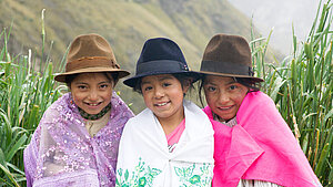 Drei Mädchen in traditioneller ecuadorianischer Kleidung lächeln in die Kamera