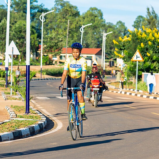 Eine junge Frau fährt im Fahrradtrikot und mit Helm auf einem Rennrad über eine Straße